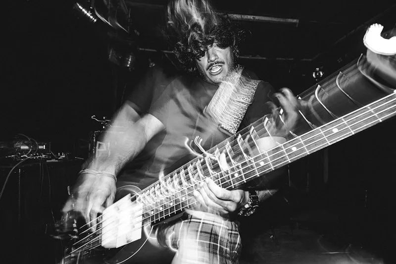 Bassist mid-strum in a blurred black-and-white live shot