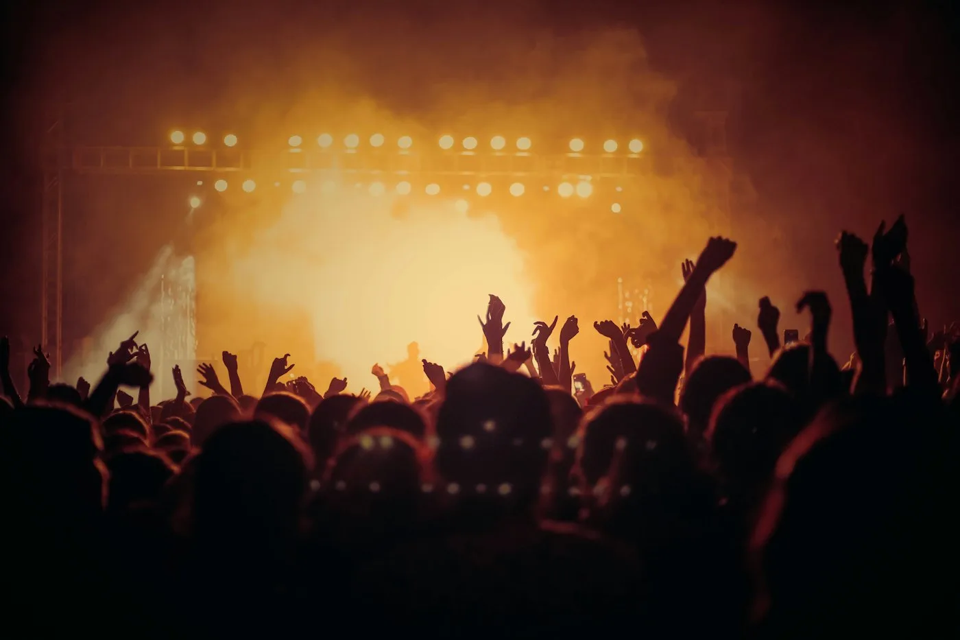Crowd with raised hands under a hazy orange stage glow